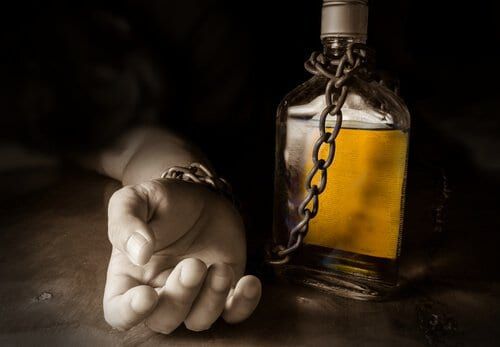 Mão acorrentada a uma garrafa de bebida alcoólica